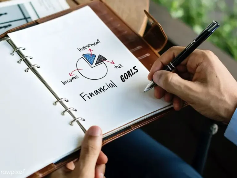 how to set financial goals - person writing financial goals in notebook at desk